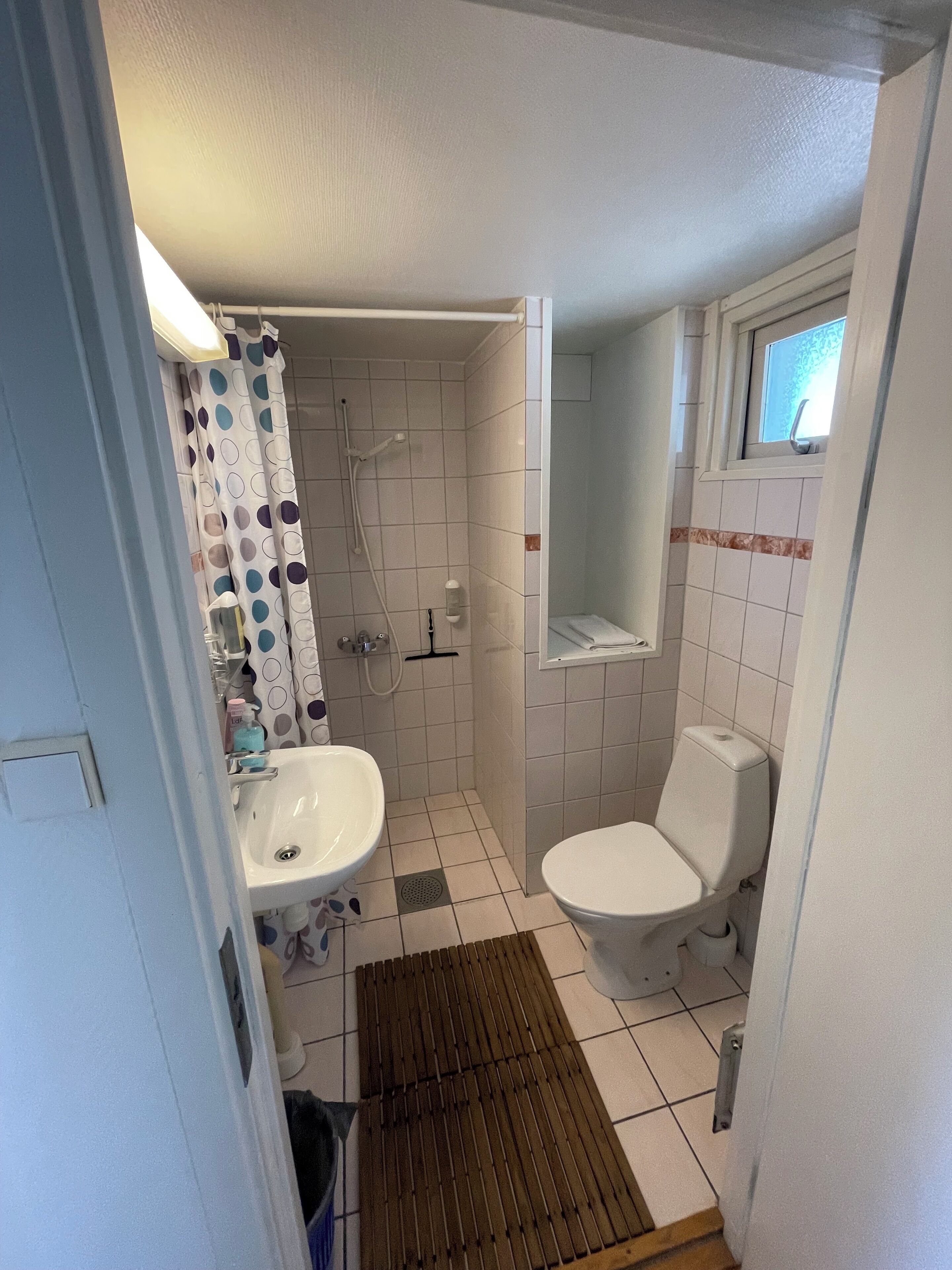 A small bathroom with a toilet, sink, shower, and a window.