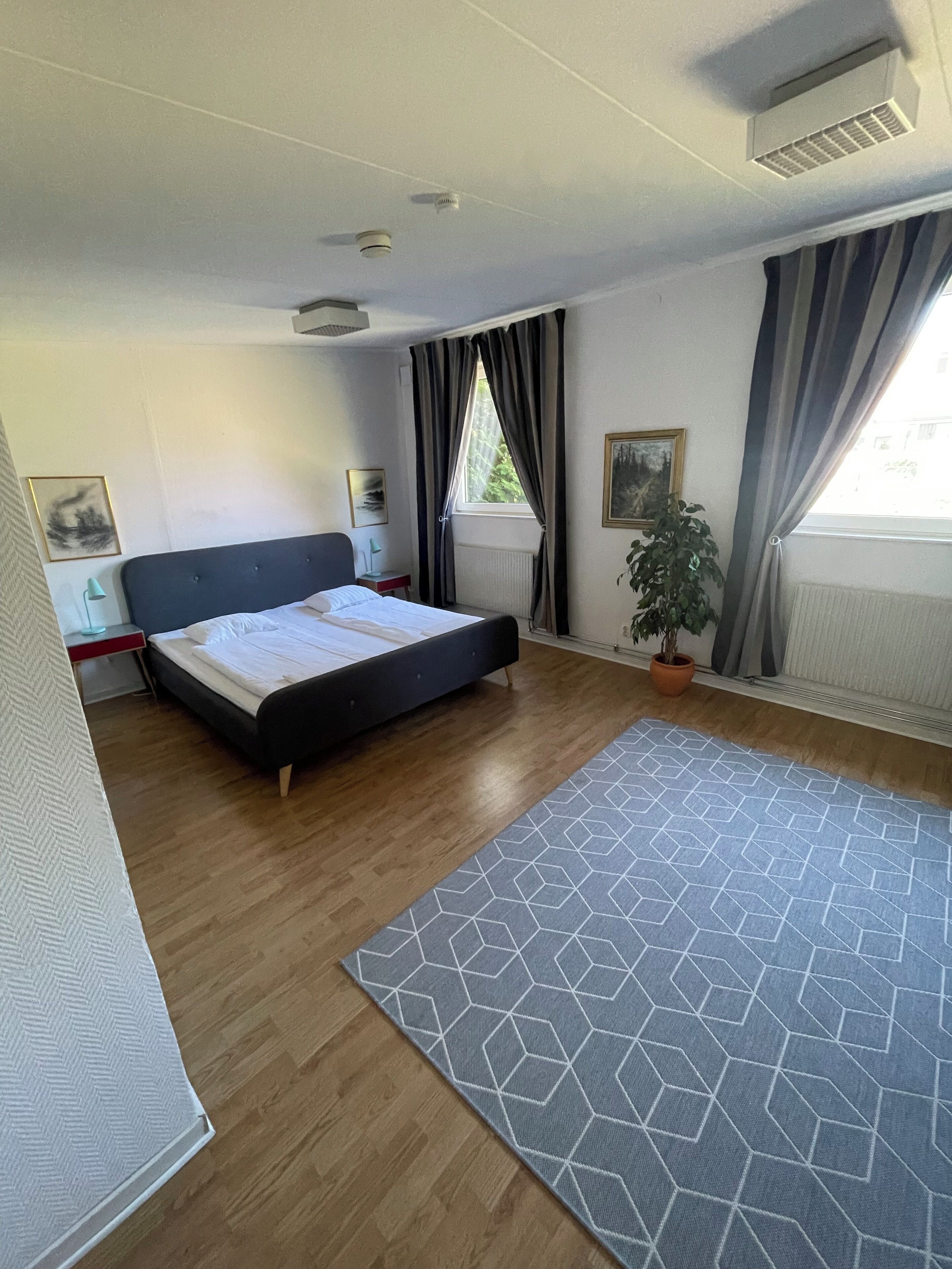 Un dormitorio moderno con cama, mesita de noche, planta en maceta y ventana con cortinas.