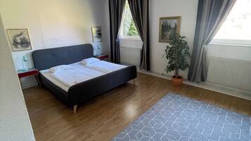 Un dormitorio moderno con cama, mesita de noche, planta en maceta y ventana con cortinas.