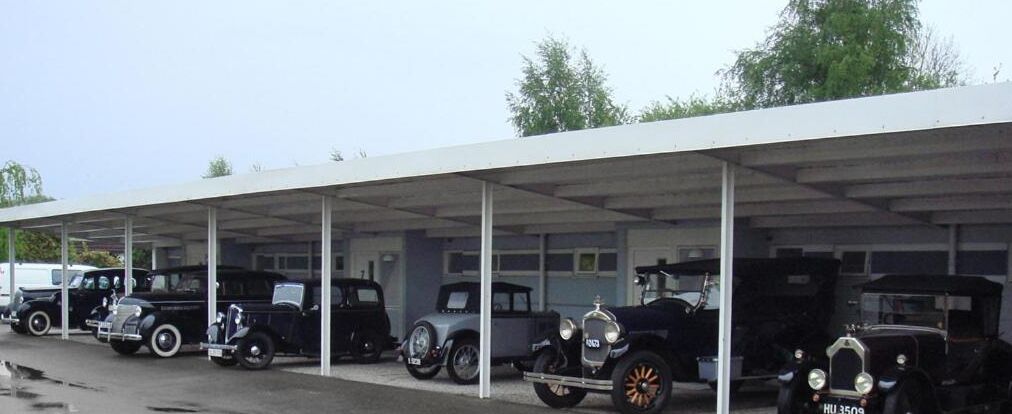 A covered parking area with vintage cars parked under a white canopy.
