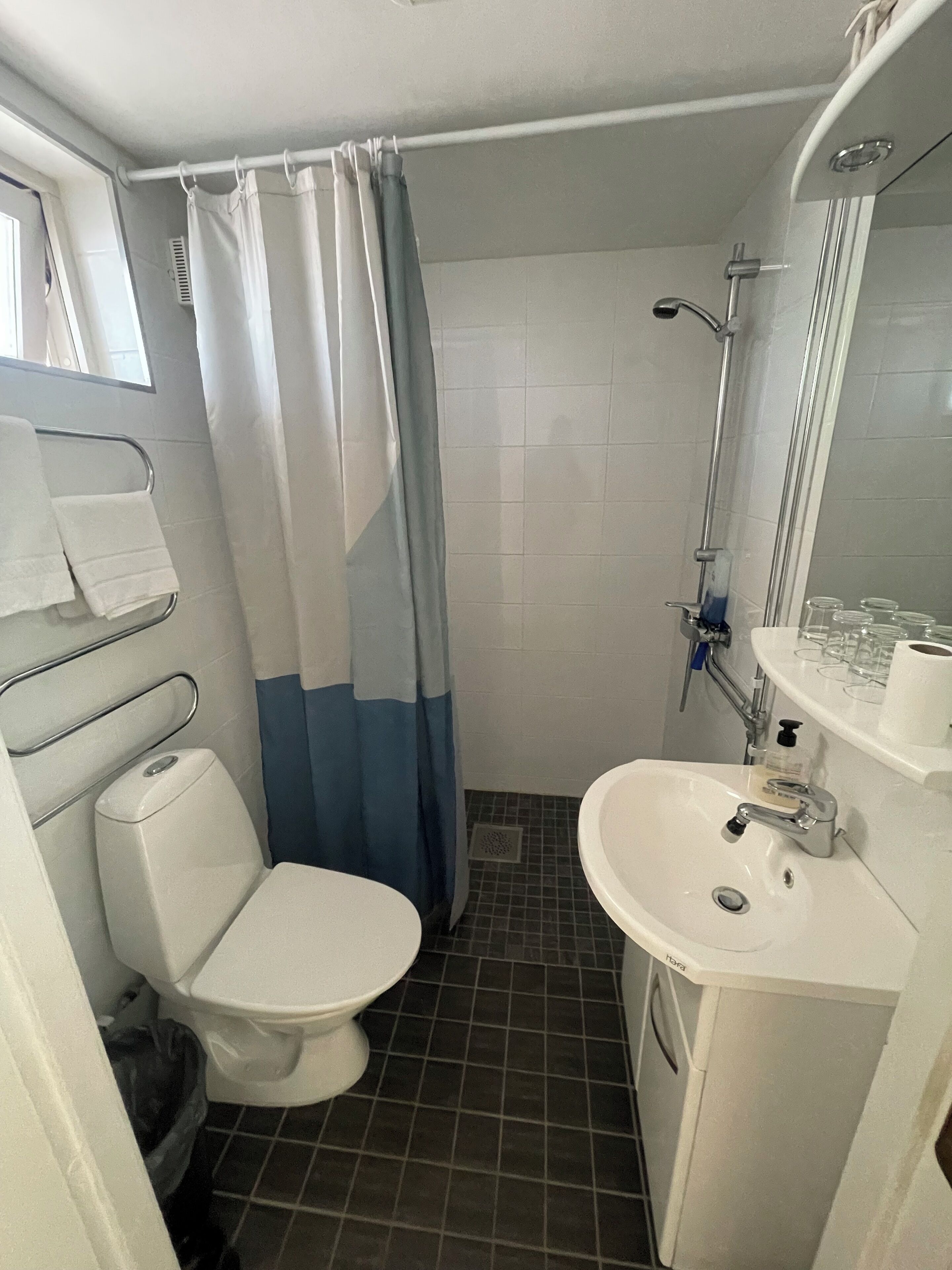 A compact bathroom with a toilet, sink, shower, and a window with a curtain.