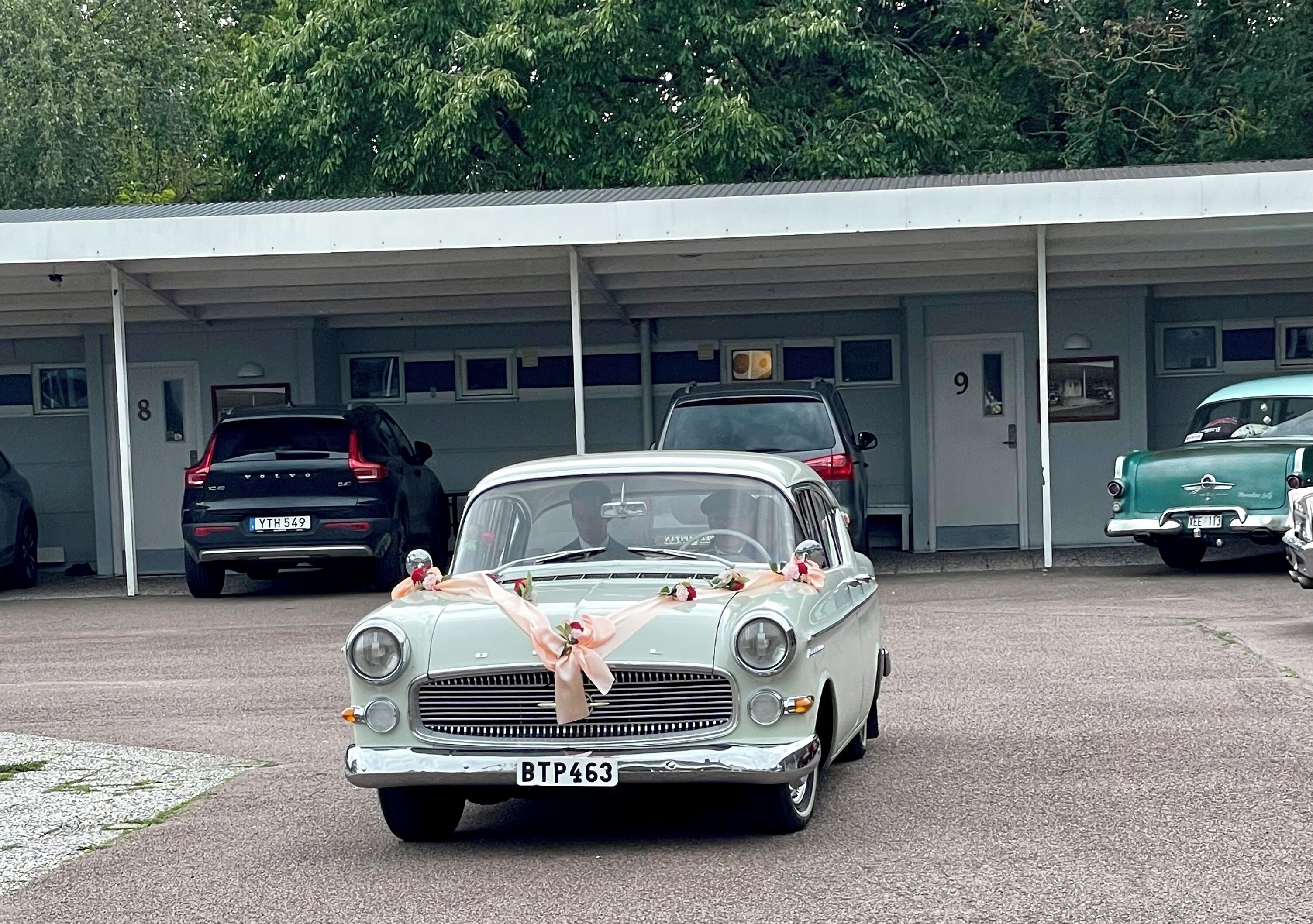 En veteranbil med registreringsnummer BTP463 står parkerad framför en byggnad vars dörrar är numrerade.