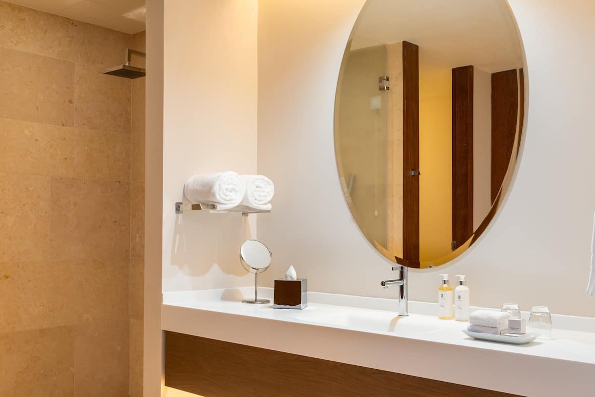 A modern bathroom with a large oval mirror, a white countertop, and a shower area.