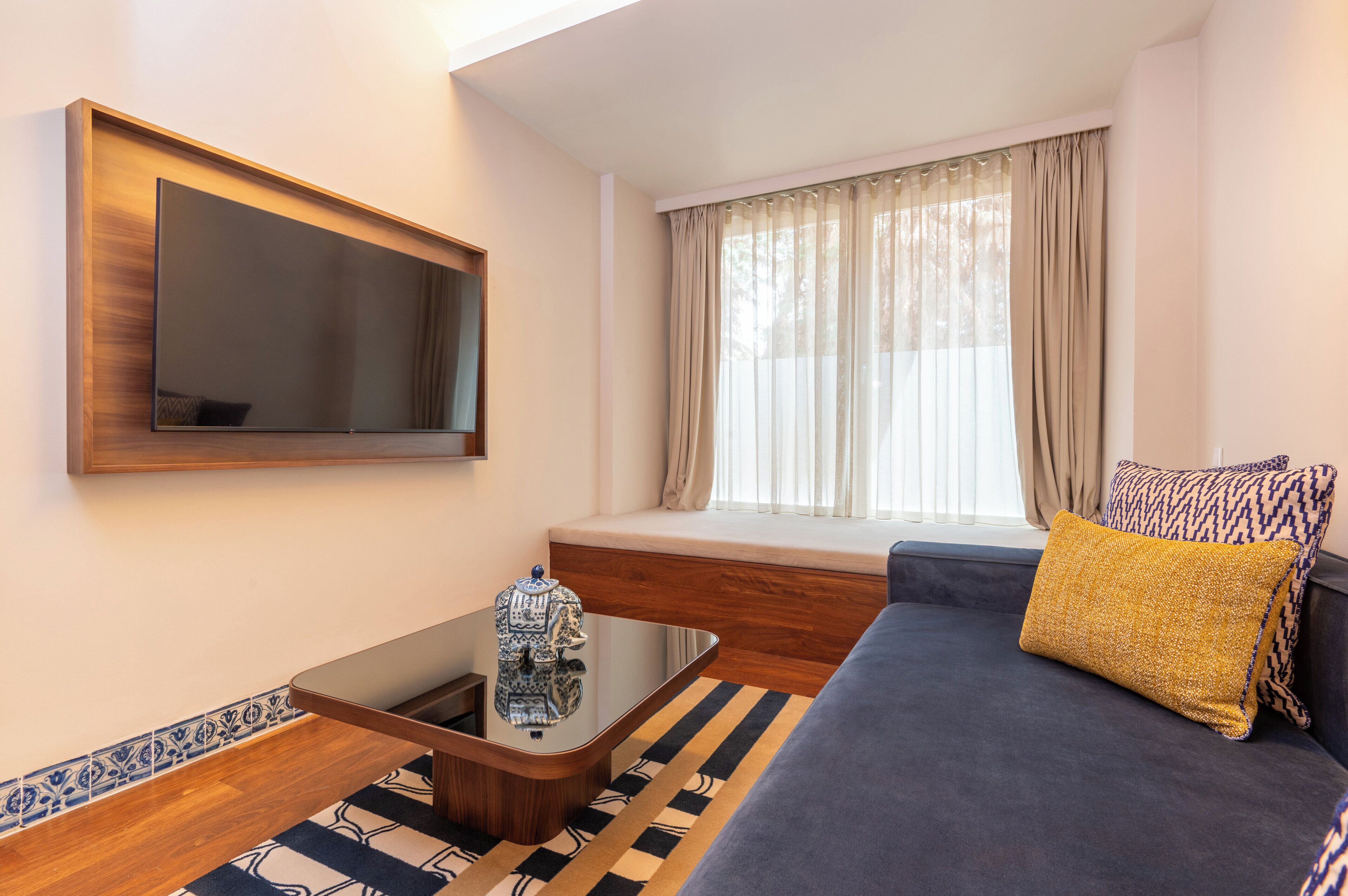 A modern living room with a sofa, a coffee table, a TV mounted on the wall, and a window with curtains.