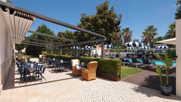 Un espace extérieur aménagé en terrasse, avec des tables et des chaises, une piscine et des parasols.