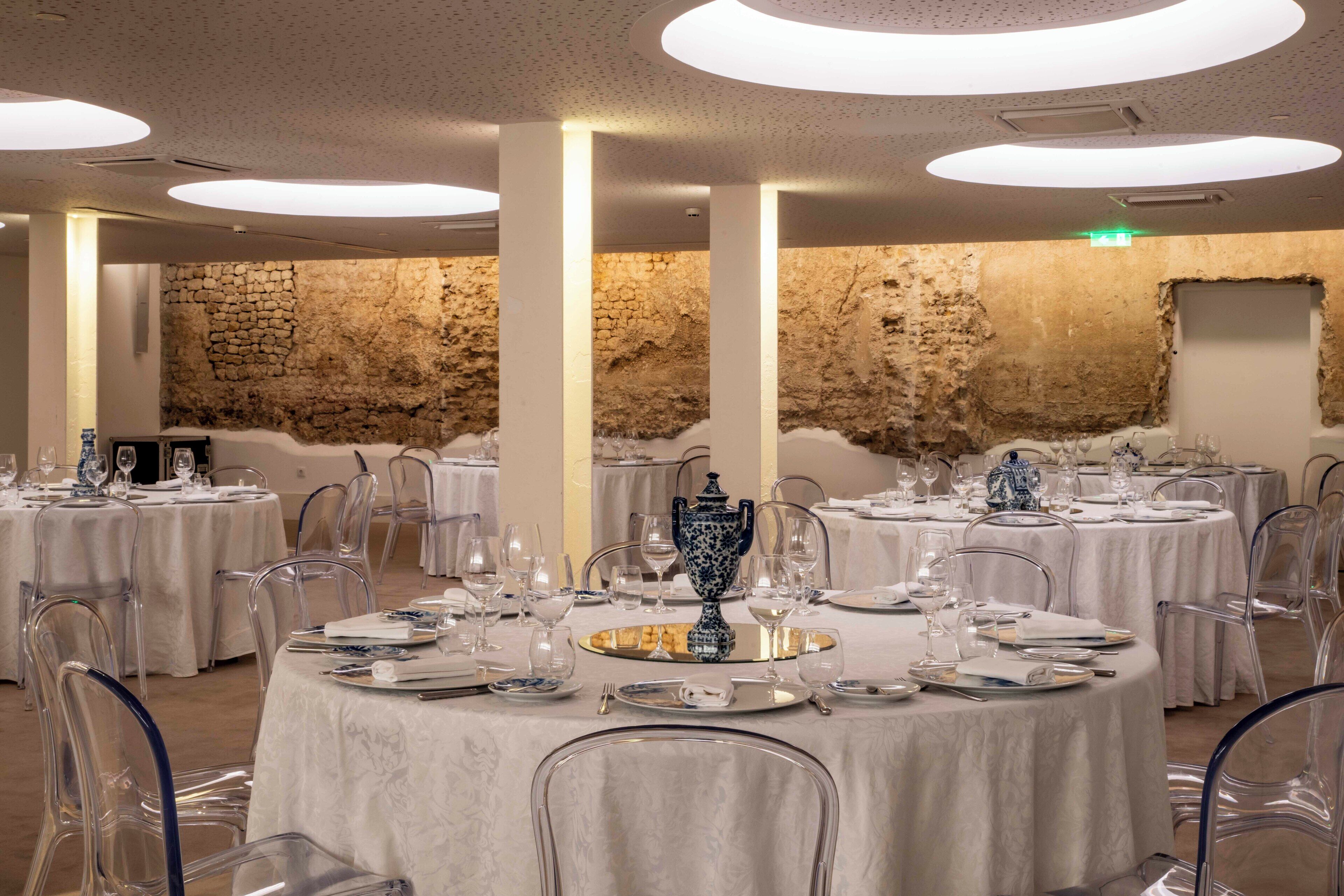 Un comedor con mesas redondas dispuestas para una comida, sillas transparentes y una pared de piedra rústica de fondo.