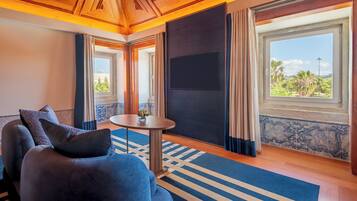Una habitación con un ventanal grande, una televisión de pantalla plana, una mesa redonda y un sofá azul con cojines.