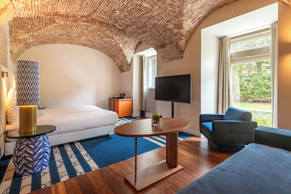 A modern room with a brick ceiling, a large window, a flat-screen TV, a sofa, a coffee table, and a patterned rug.