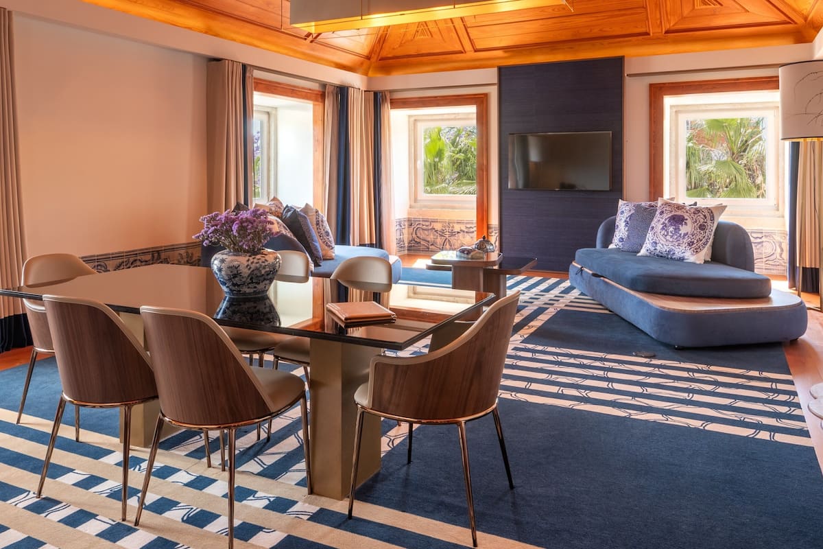 A modern living room with a wooden ceiling, a dining area with a table and chairs, a blue sofa, and a flat-screen TV mounted on the wall.