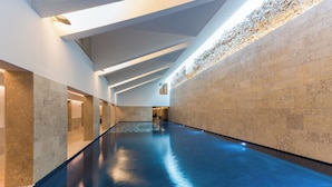 Une longue piscine intérieure étroite, dotée d’un sol réfléchissant et entourée de murs à motifs texturés.