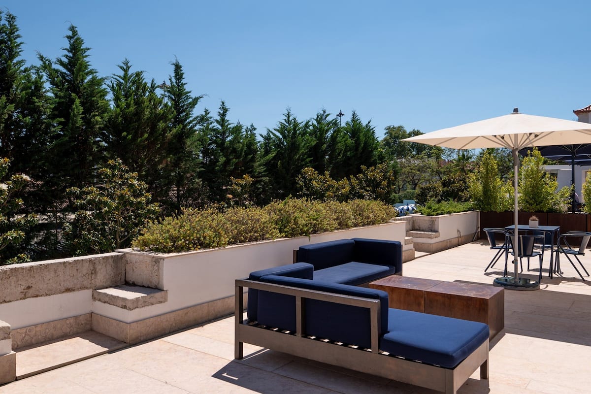 An outdoor patio area with a seating arrangement, including a sofa and chairs, and a table with an umbrella.