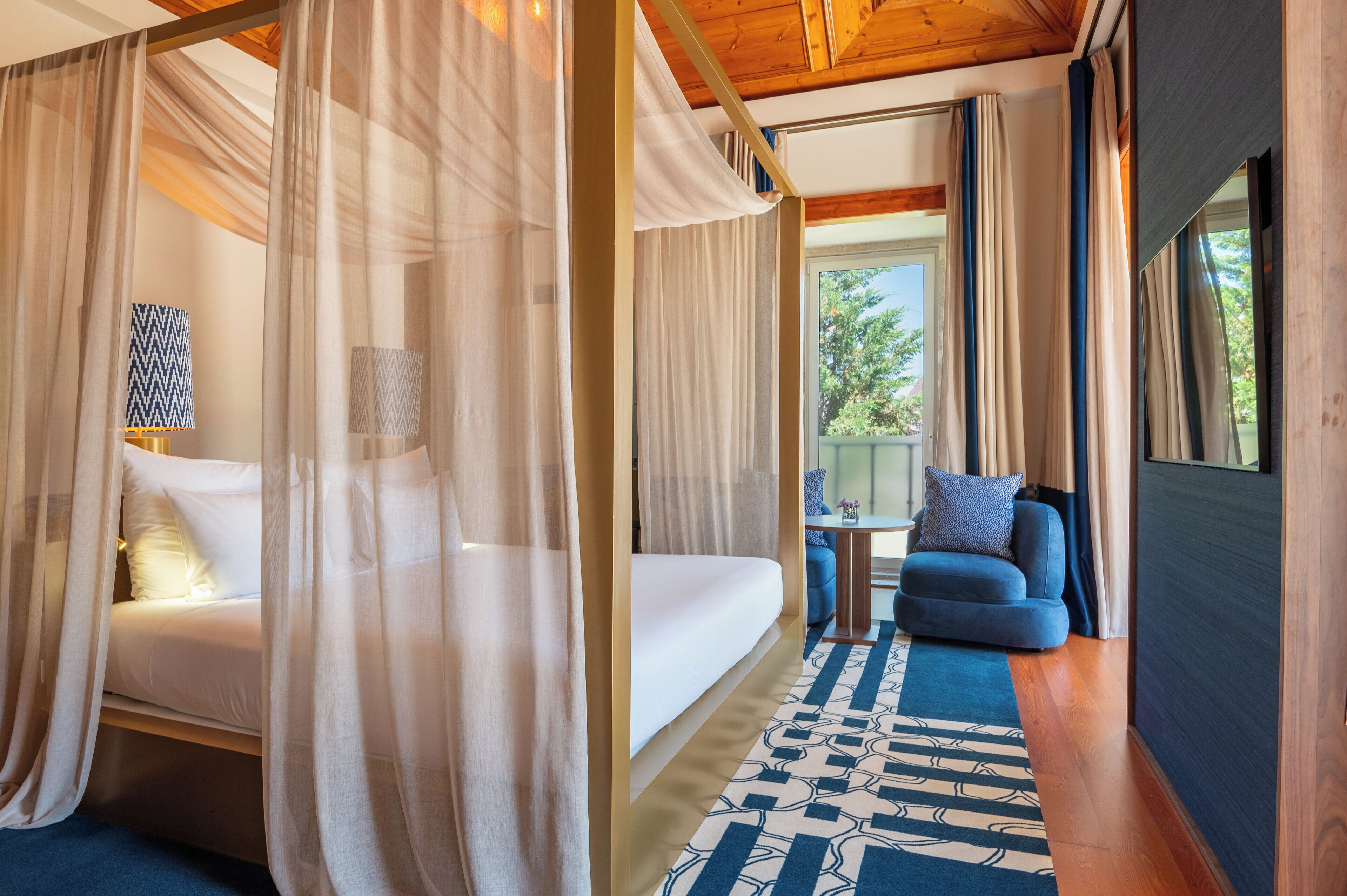 Een slaapkamer met een bed, een tafeltje, een bank en een groot raam.