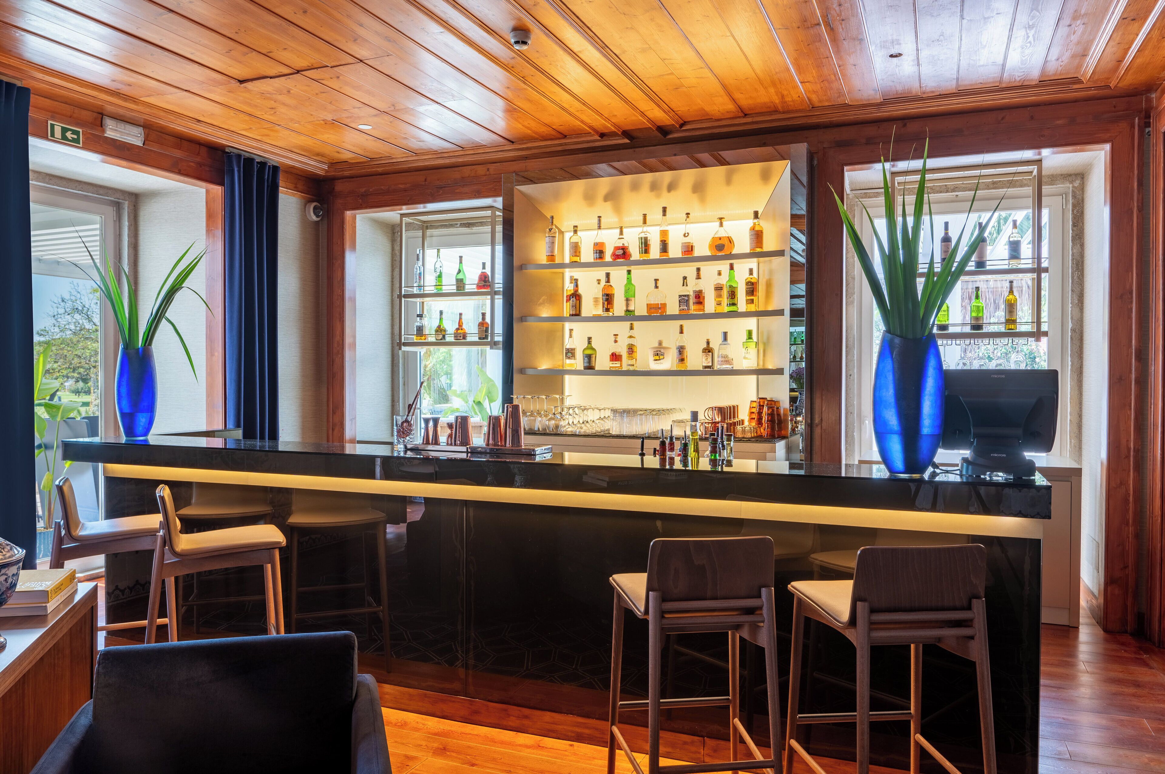 Een bar met houten plafond, flessenkasten en barstoelen.