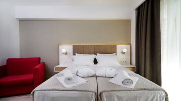 Una habitación de hotel con una cama, dos mesitas de noche, un sillón rojo y una ventana con cortinas.