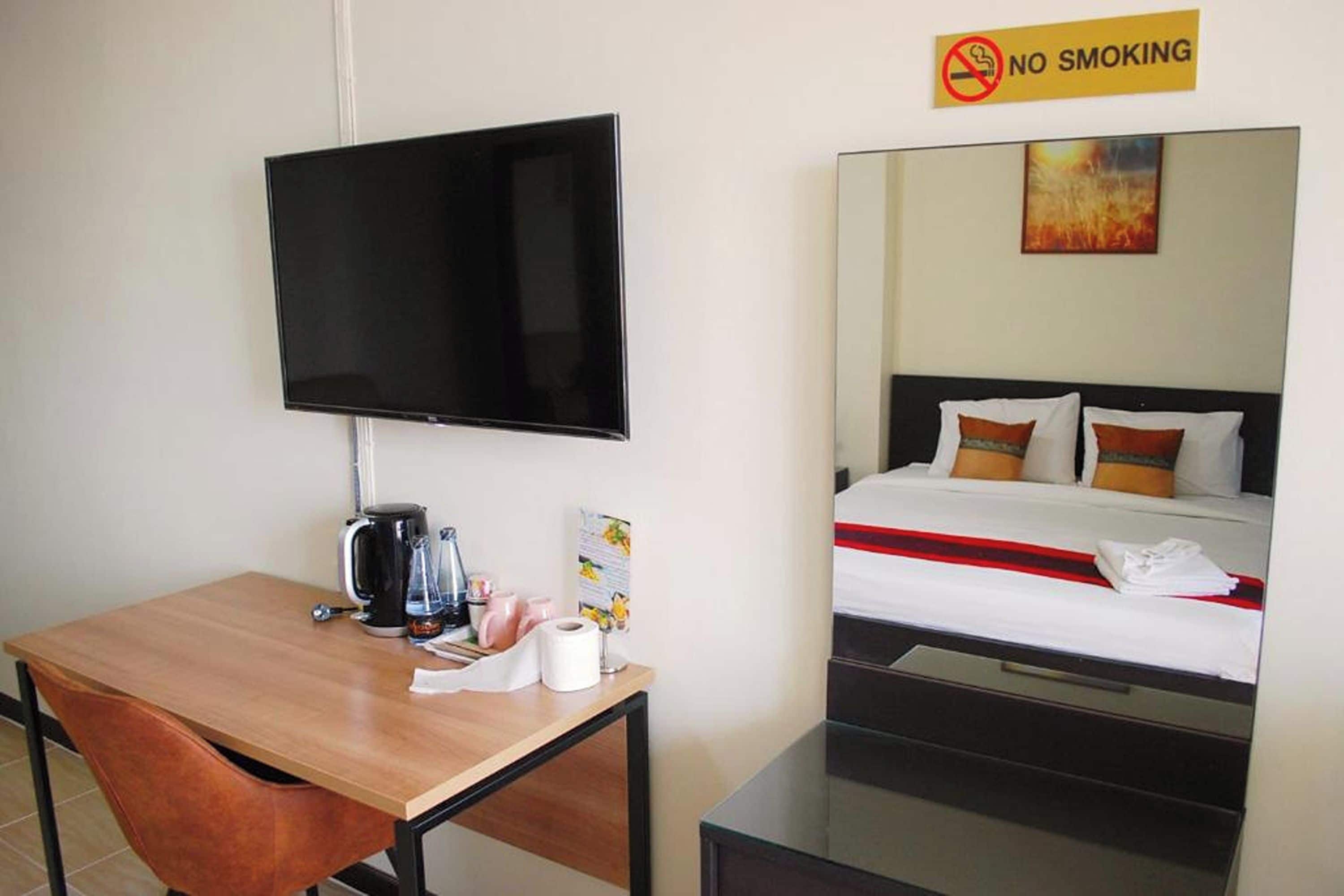 A hotel room with a flat-screen TV mounted on the wall, a wooden desk with a coffee maker, and a bed with a red and white striped blanket.
