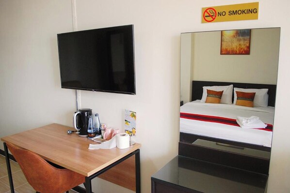 Quarto de hotel com televisão de tela plana na parede, escrivaninha de madeira com cafeteira e cama com cobertor listrado em vermelho e branco.