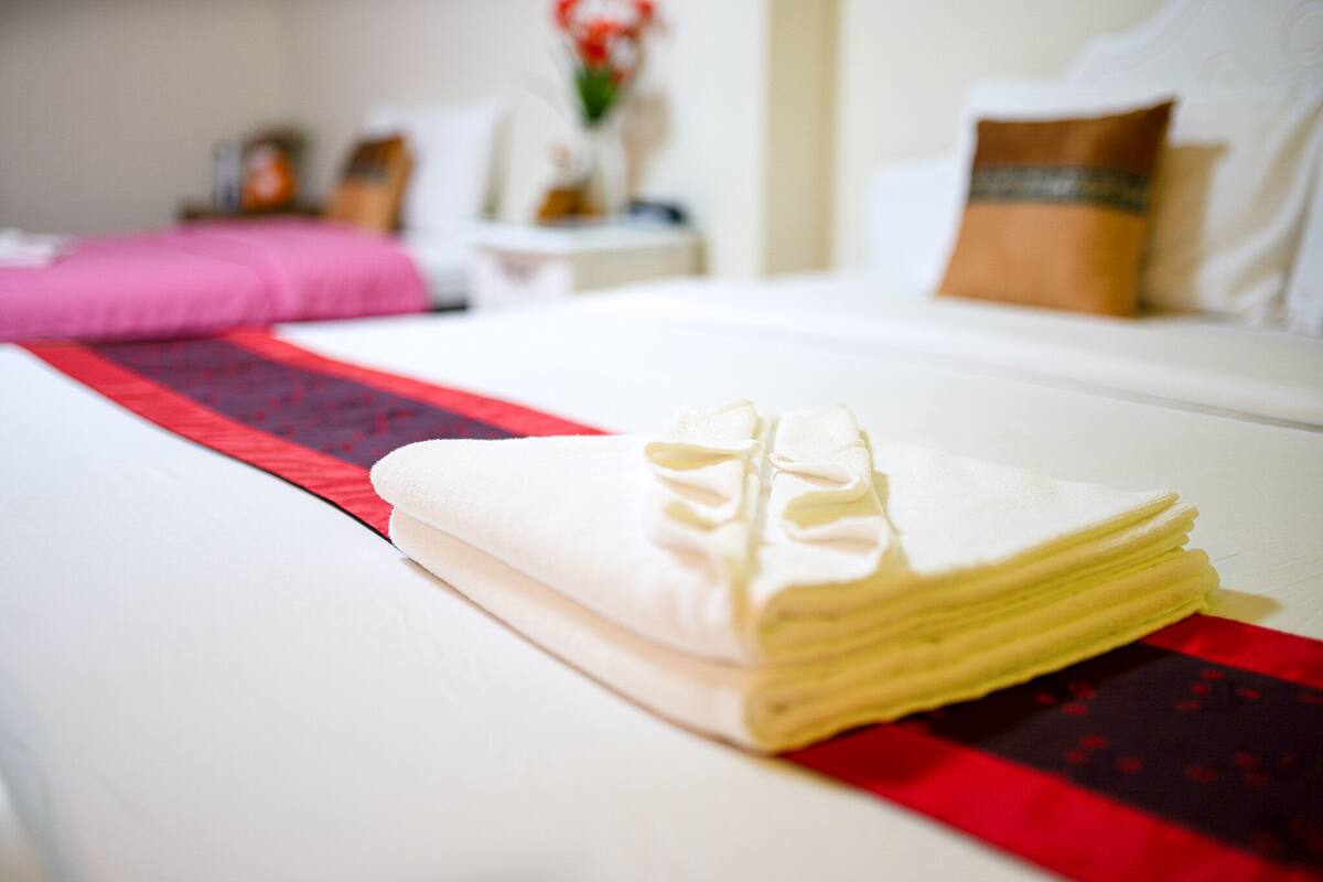 Una cama bien hecha con una toalla blanca doblada y un corredor rojo y negro estampado.