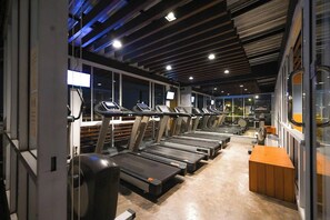 A gym with multiple treadmills aligned in rows, a wooden bench, and a wall-mounted TV screen. - Witchuwan Sport & Spa Apartel (Bangkok)