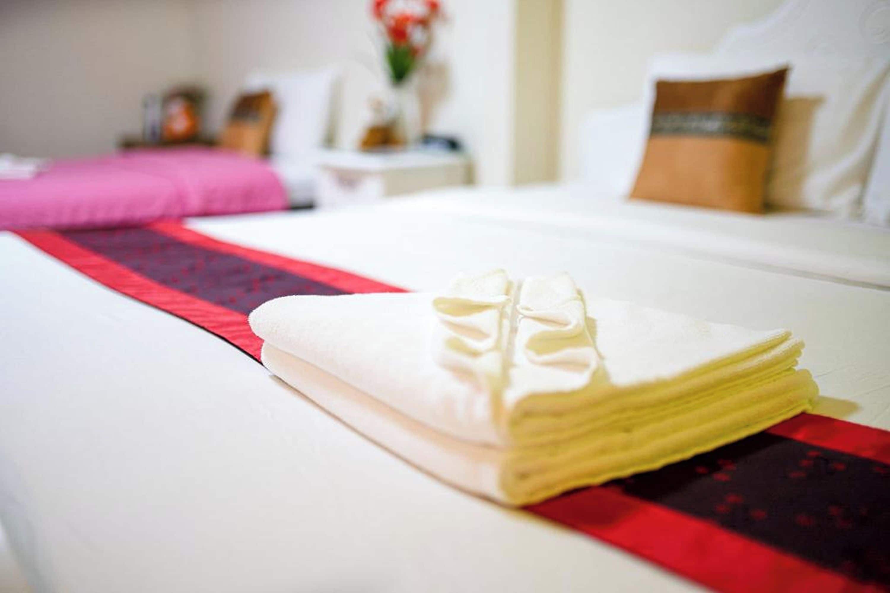 Cama bem arrumada com toalha dobrada e edredom vermelho e preto.