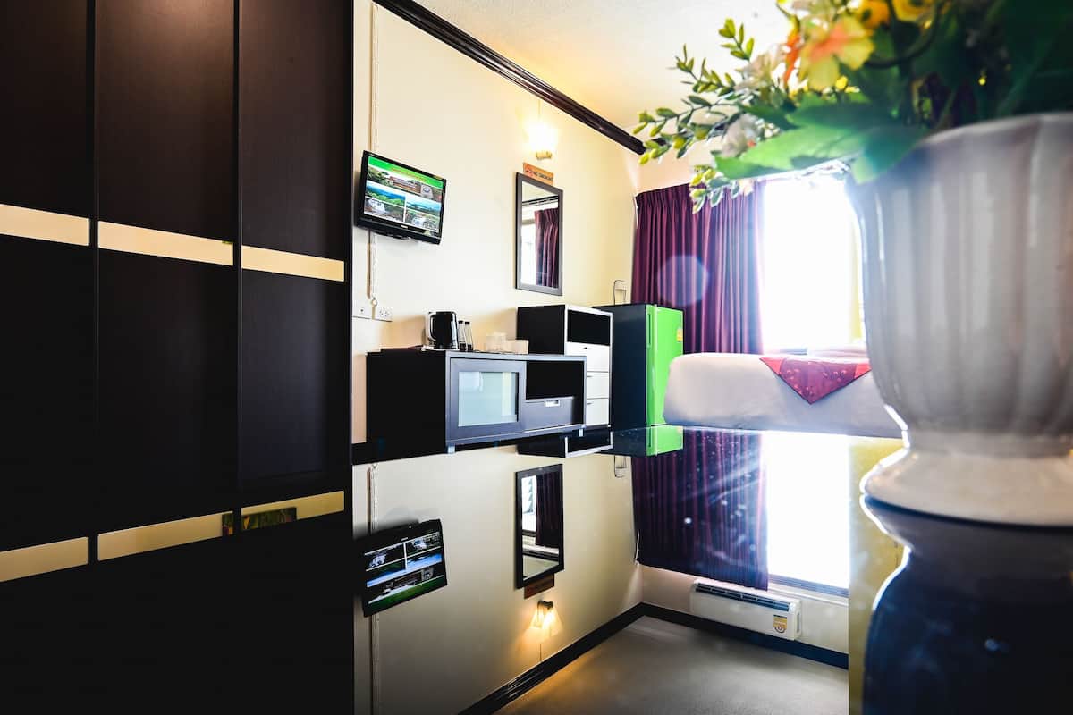 Habitación de hotel con televisor de pantalla plana montado en la pared, una pequeña kitchenette con microondas y un ventanal con cortinas.