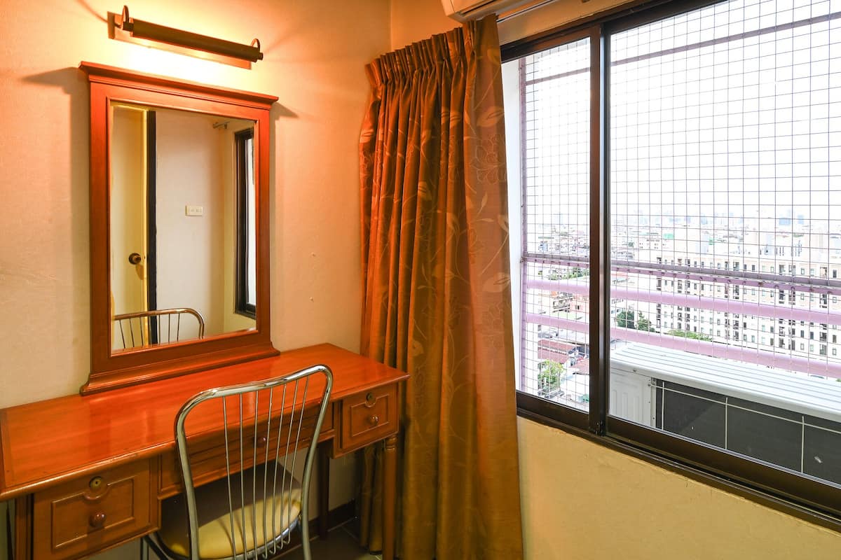 Una habitación con un escritorio de madera, una silla, un espejo y un ventanal con vistas a edificios.