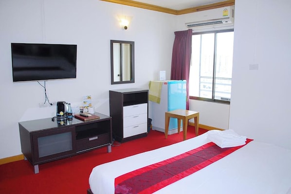 Habitación de hotel con cama, escritorio con silla, televisión, espejo y unidad de aire acondicionado.