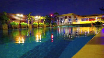 A swimming pool with a reflection of lights, palm trees, and a building with a glass facade.