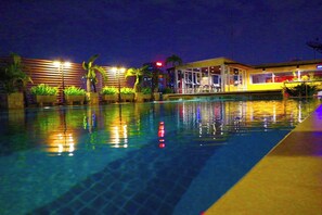 A swimming pool with a reflection of lights, palm trees, and a building with a glass facade. - Witchuwan Sport & Spa Apartel (Bangkok)