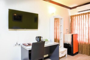 A hotel room with a desk, chair, a flat-screen TV mounted on the wall, a mini-fridge, and a bed with curtains. - Witchuwan Sport & Spa Apartel (Bangkok)