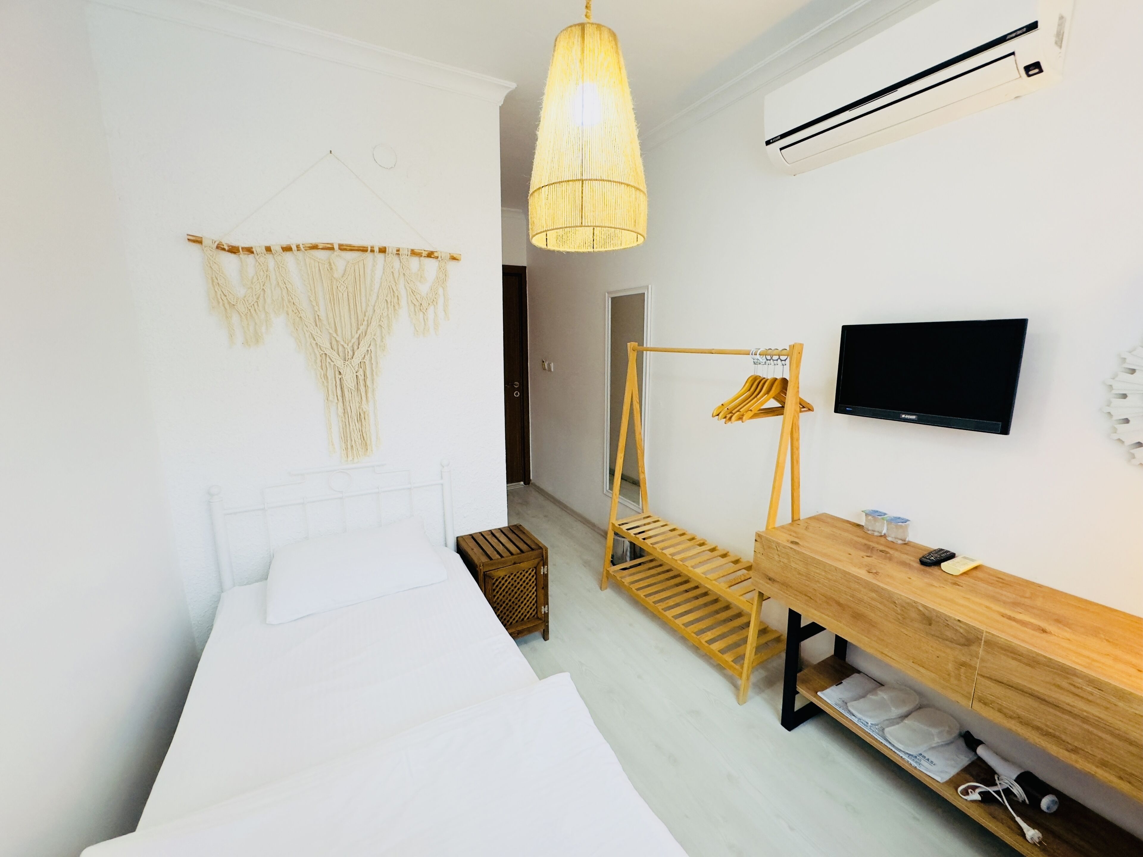 Un dormitorio con una cama, una mesita de noche de madera, un televisor, un adorno colgante de macramé y un equipo de aire acondicionado.