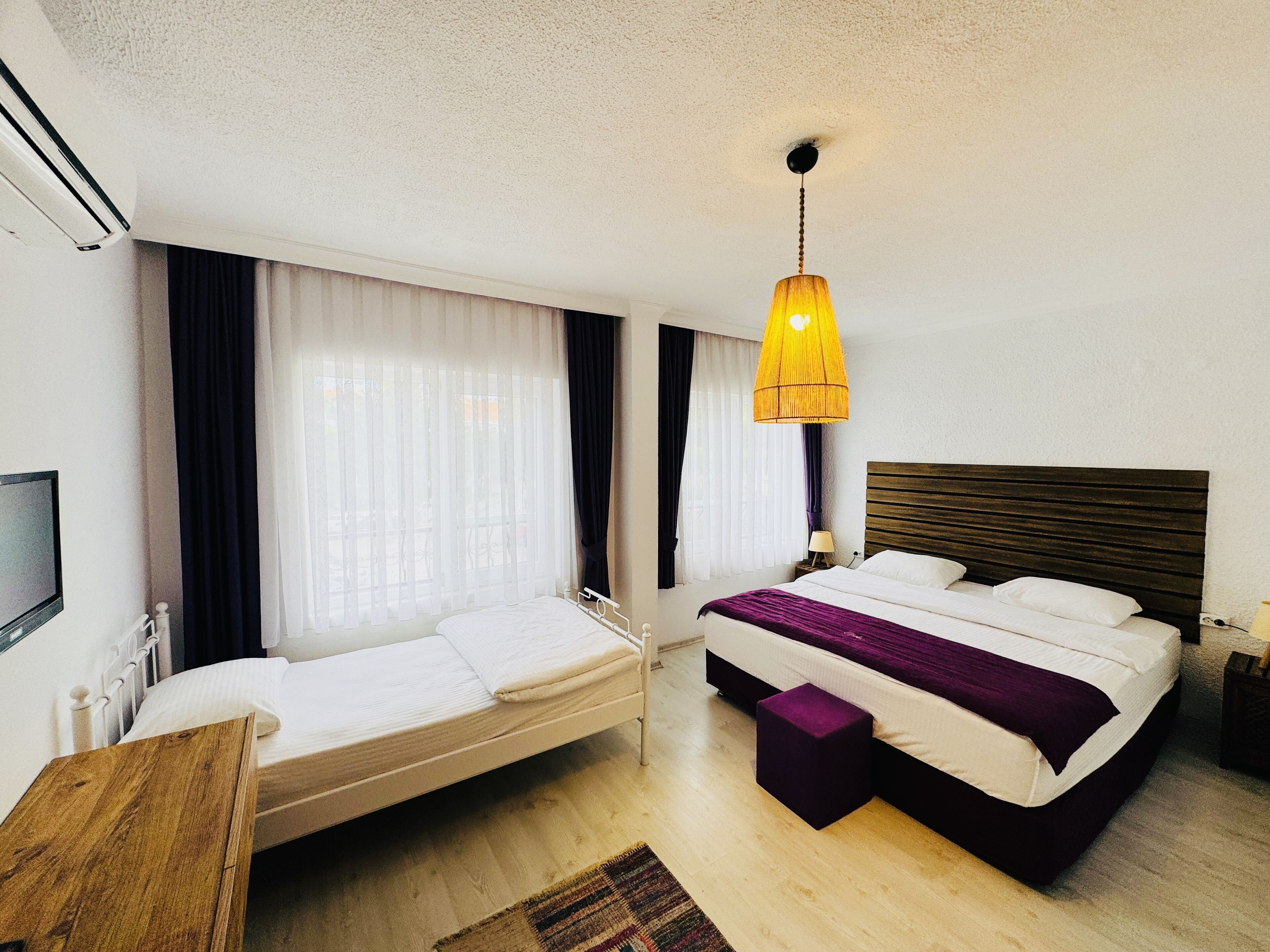 A hotel room with a bed, a small desk, a TV, and a window with curtains.