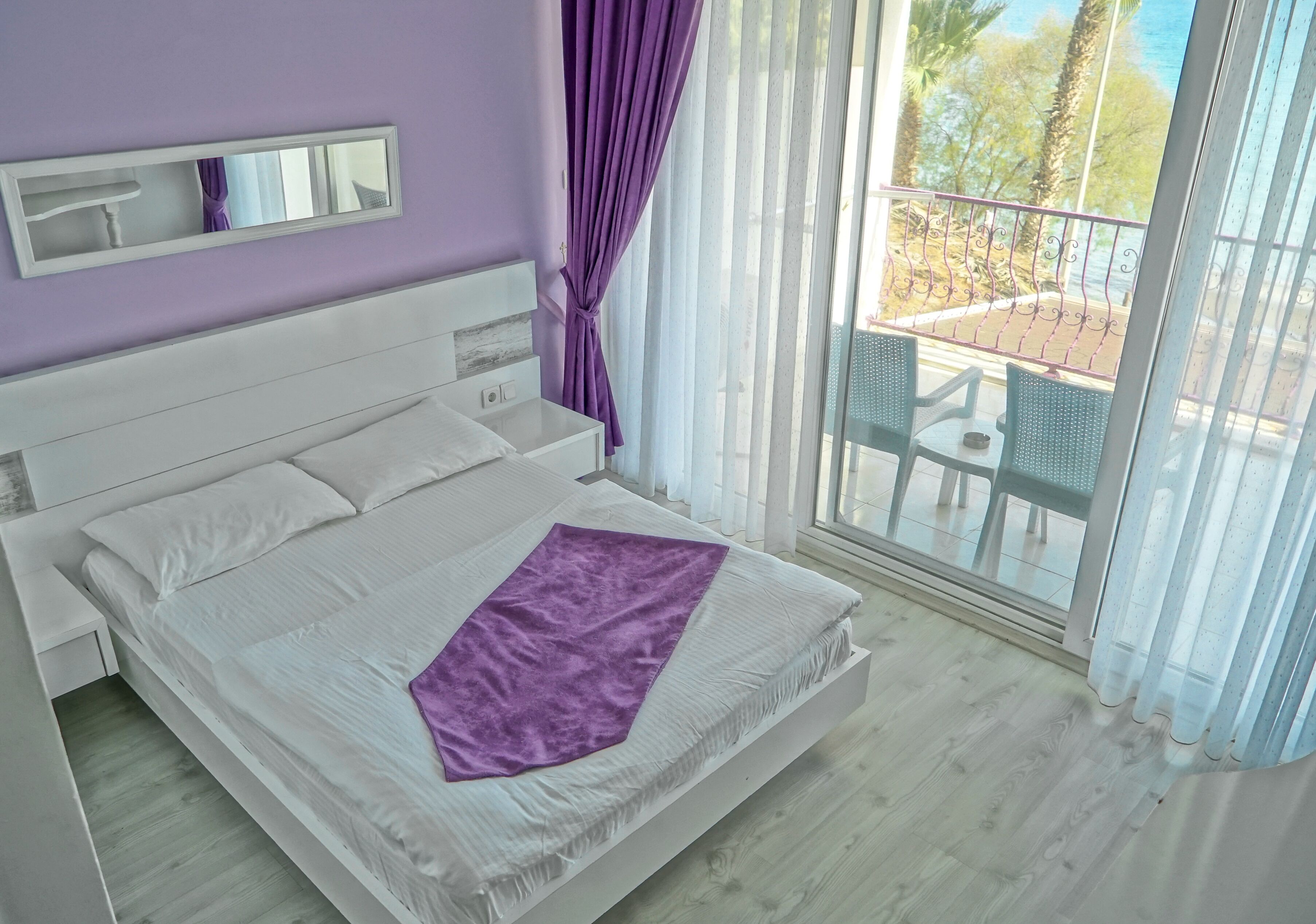 A bedroom with a large bed, a nightstand, a window with curtains, and a view of the outside.