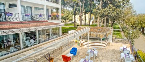 A hotel with outdoor seating, a covered area, and a view of trees and buildings.