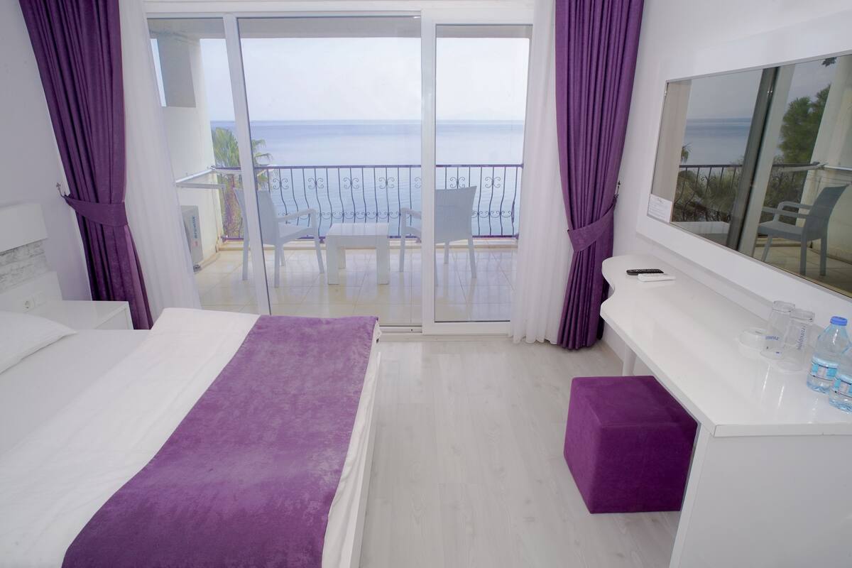 A hotel room with a balcony, a bed, a small table, and a window.