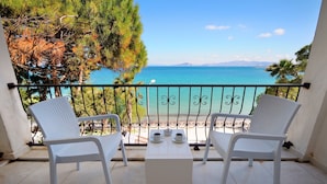 A balcony with two white wicker chairs and a small table, overlooking a clear blue sea and distant mountains. - Fuda Hotel (Datça)