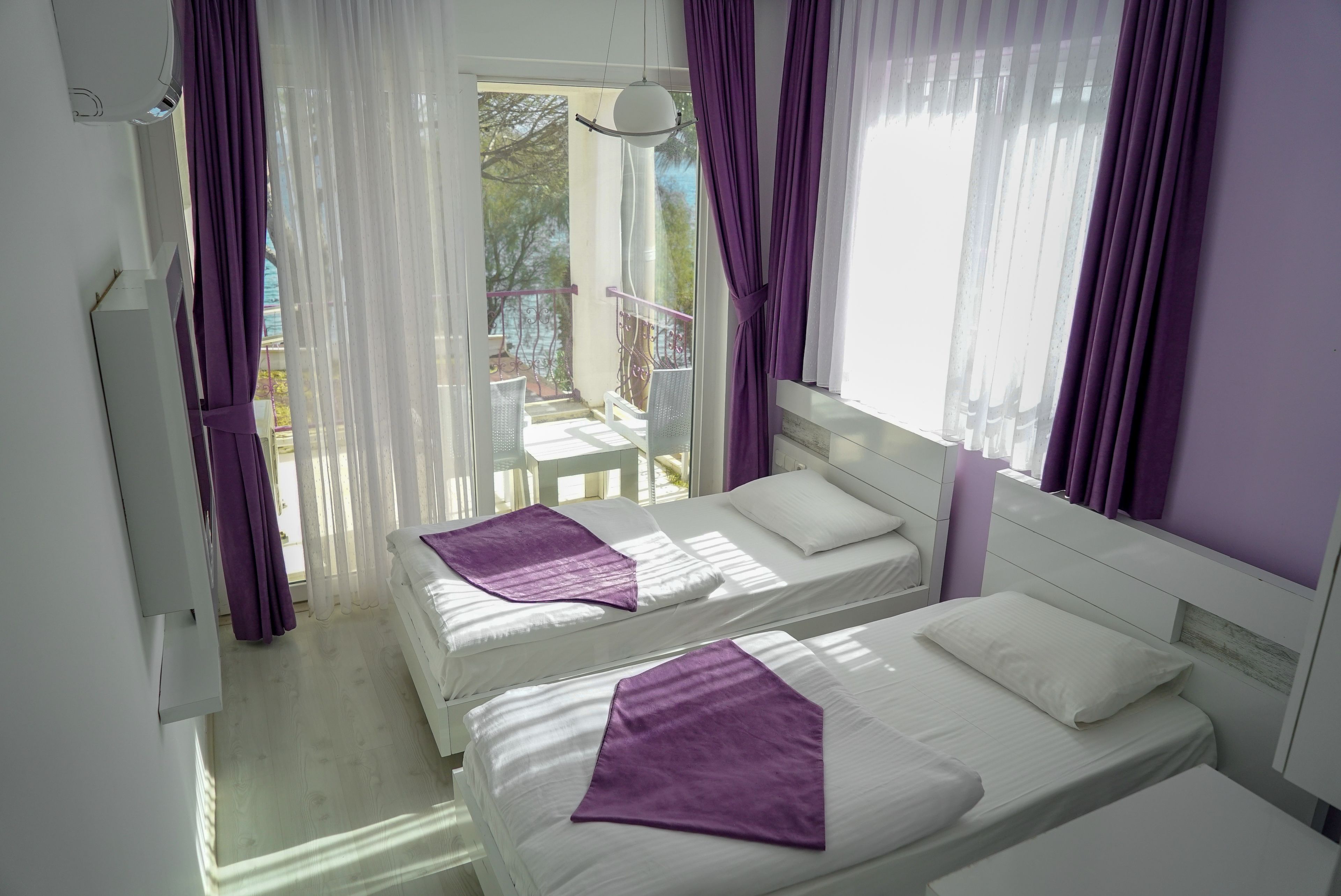 A room with two beds, white bedding, purple bedspreads, and a balcony with a railing.