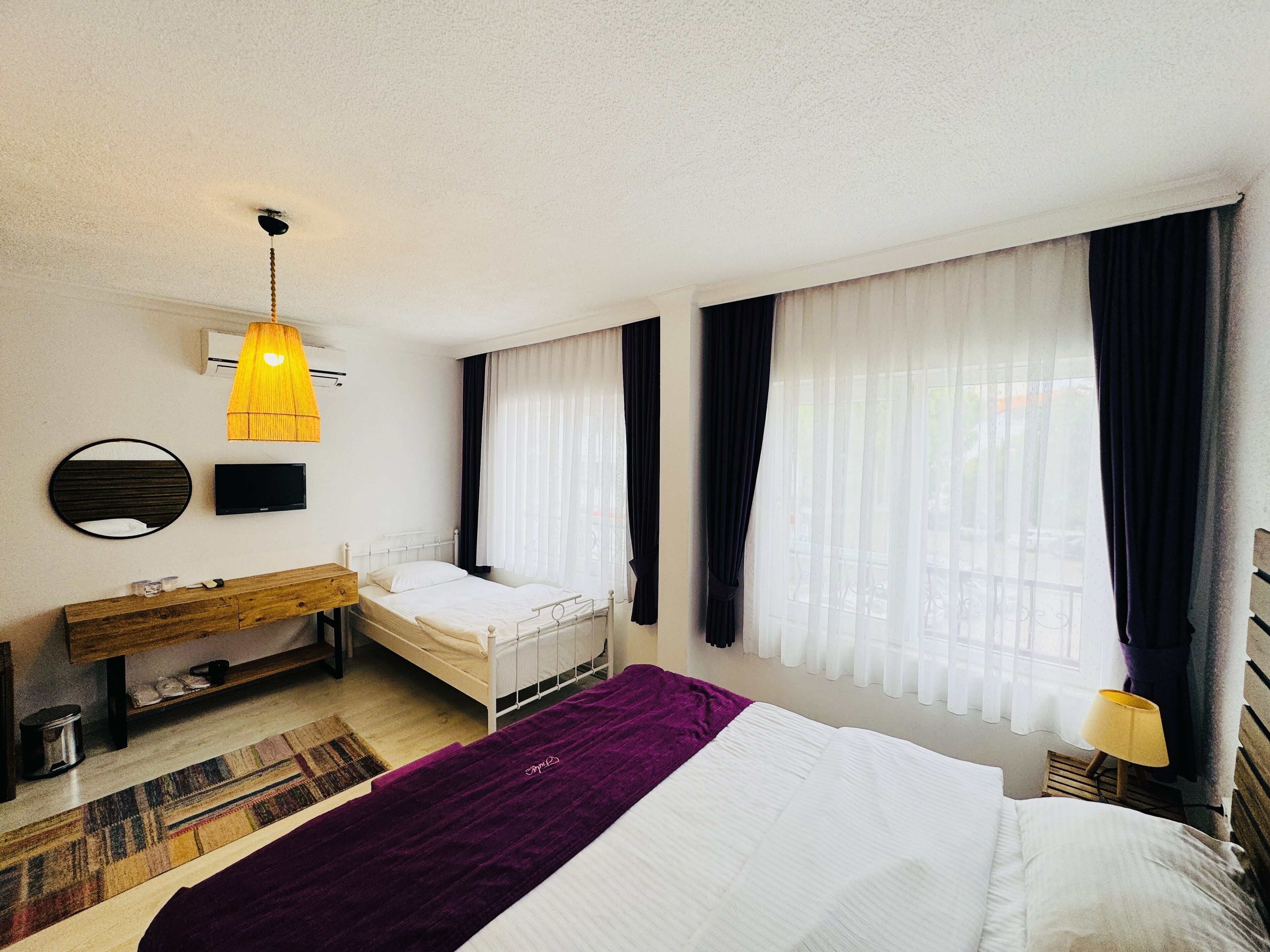 A bedroom with a bed, a bedside table, a TV, a mirror, and a window with curtains.