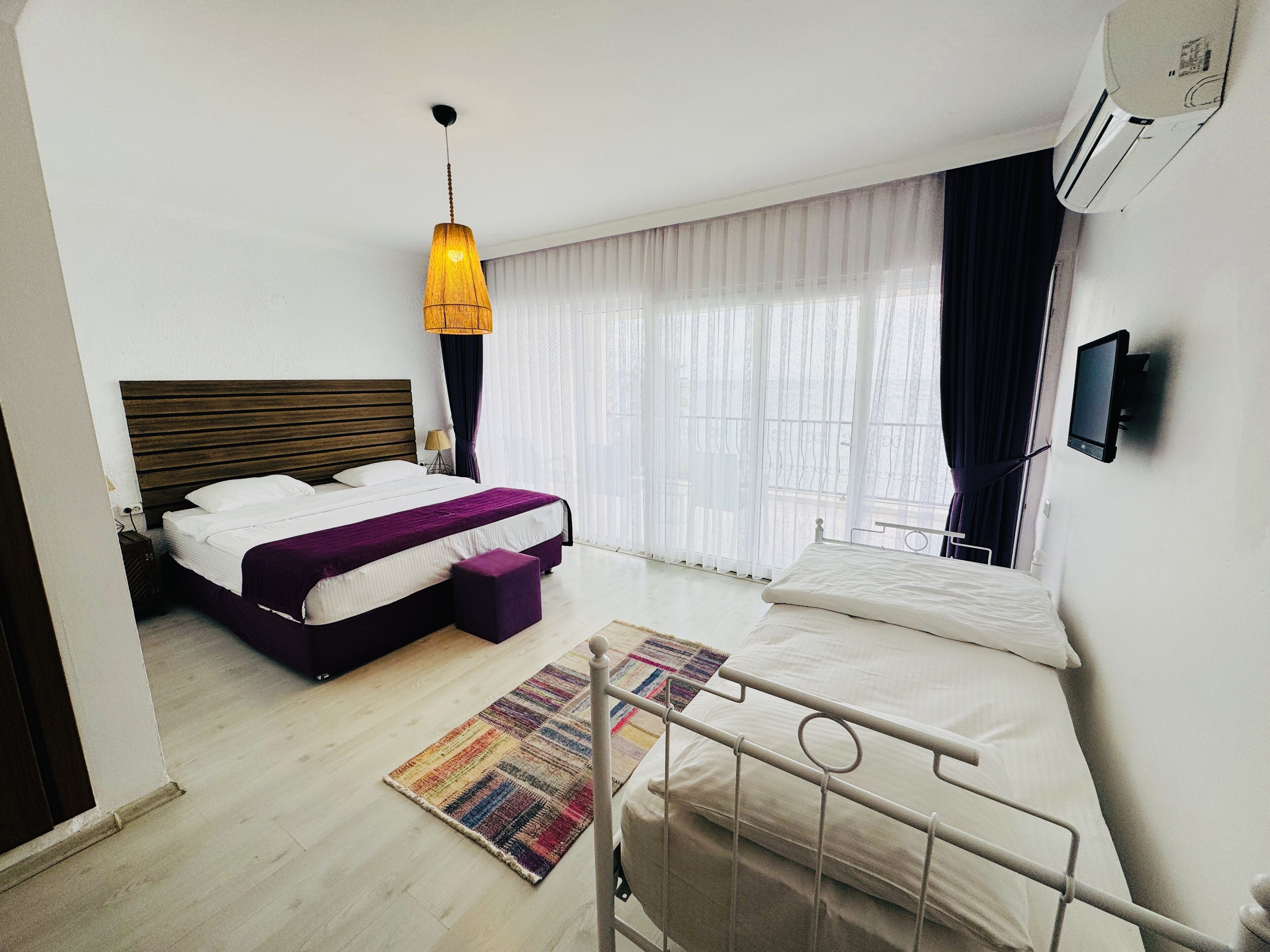 Una habitación de hotel con una cama, una mesita de noche, una lámpara, una ventana con cortinas, un televisor y un equipo de aire acondicionado.