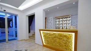 A reception area with a glass door entrance, a reception desk with a decorative back panel, and a wall-mounted key rack. - Fuda Hotel (Datça)