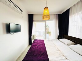 A hotel room with a bed, a television on the wall, and a balcony with a view.
