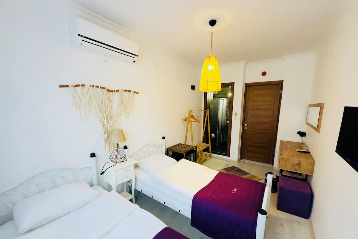 A hotel room with a bed, bedside tables, a lamp, a hanging macrame wall decoration, a wardrobe, and a television.