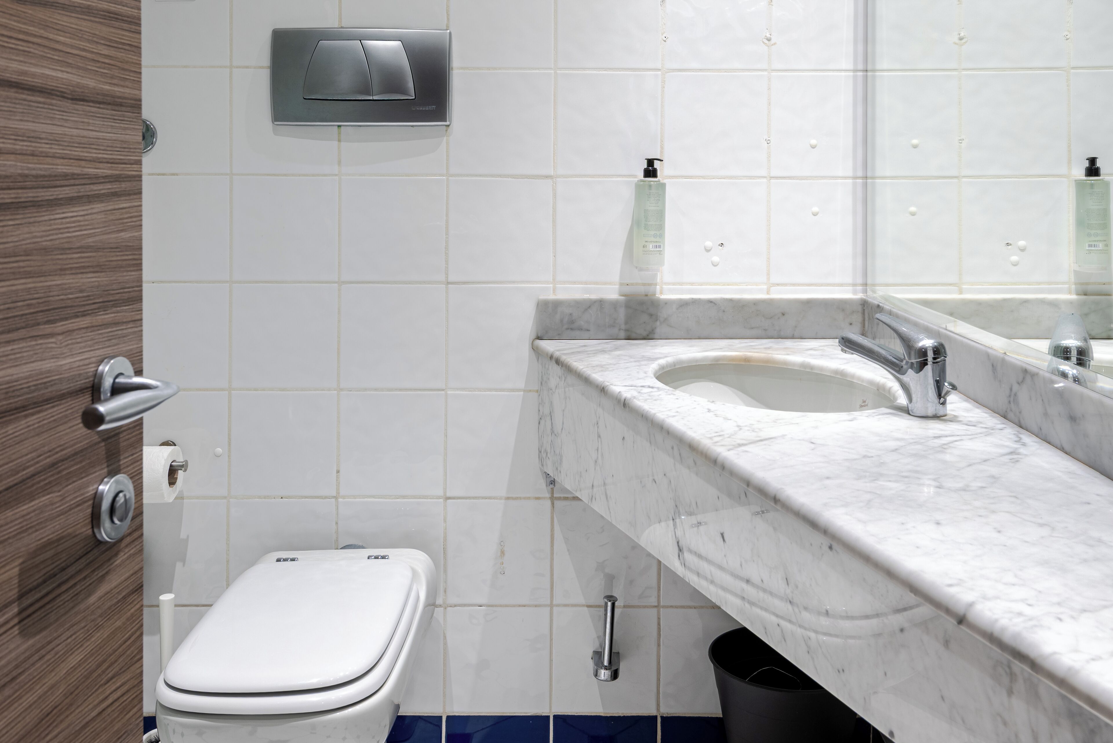 A bathroom with a toilet, sink, mirror, and hand dryer.