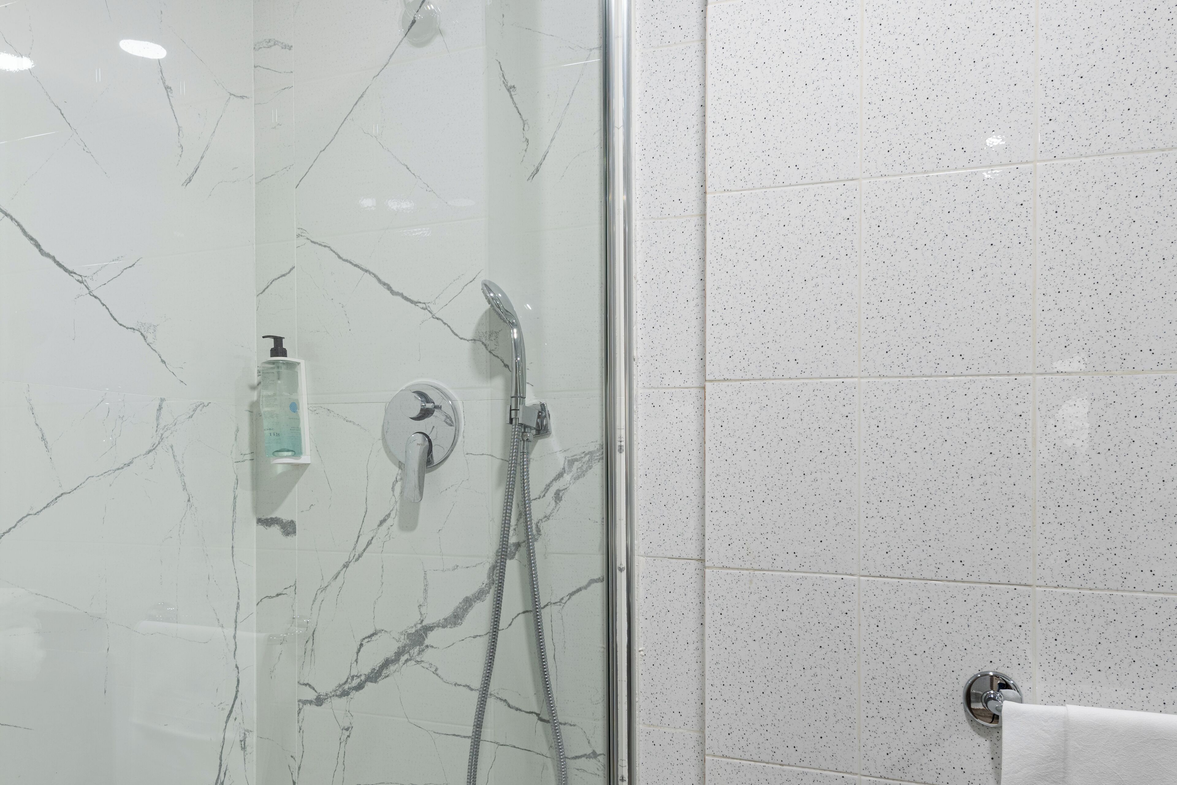 Une salle de bain dotée d’une douche à parois de verre, de murs en marbre blanc et d’un sol carrelé.