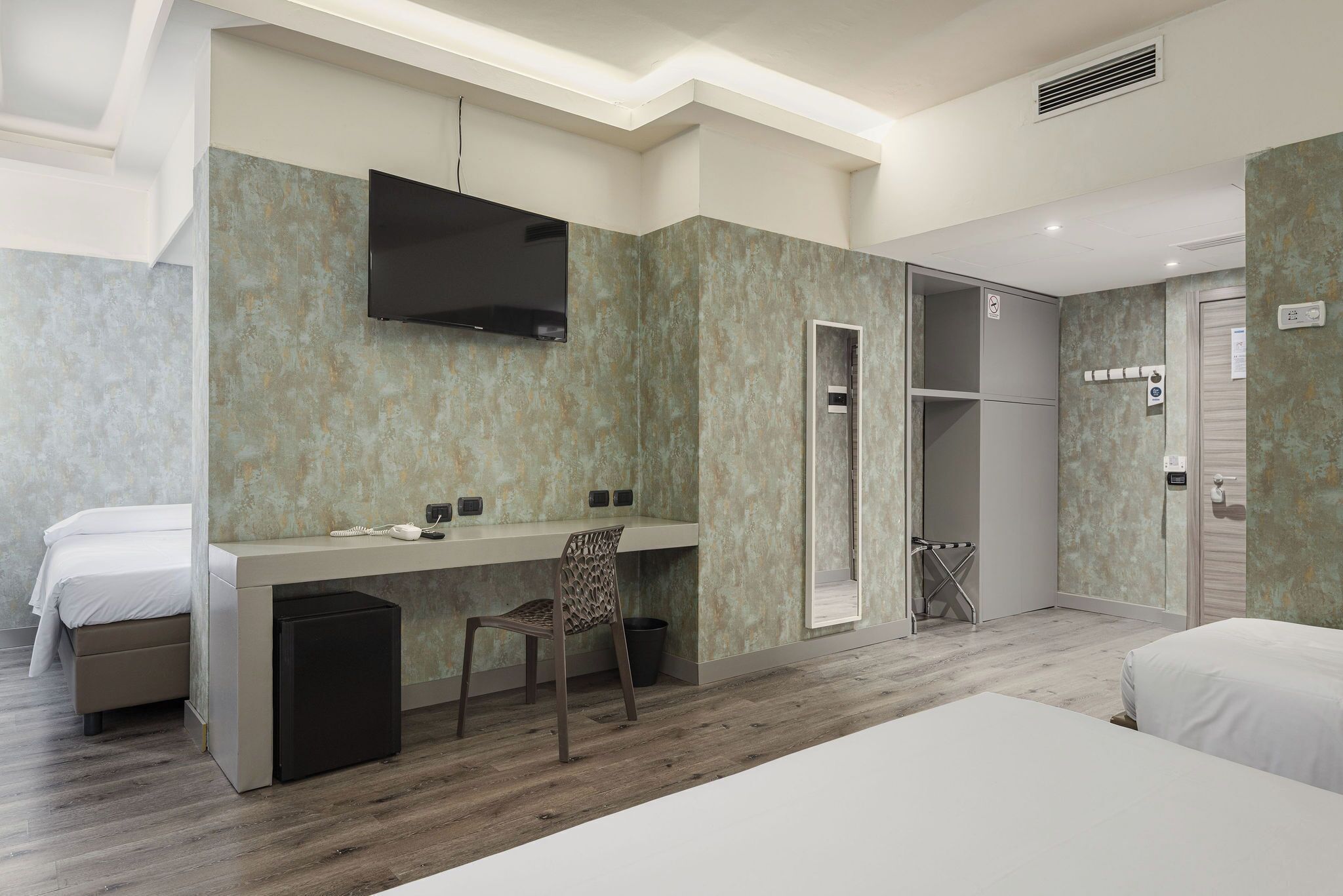 Una habitación de hotel moderna con cama, escritorio, silla, televisor y armario.