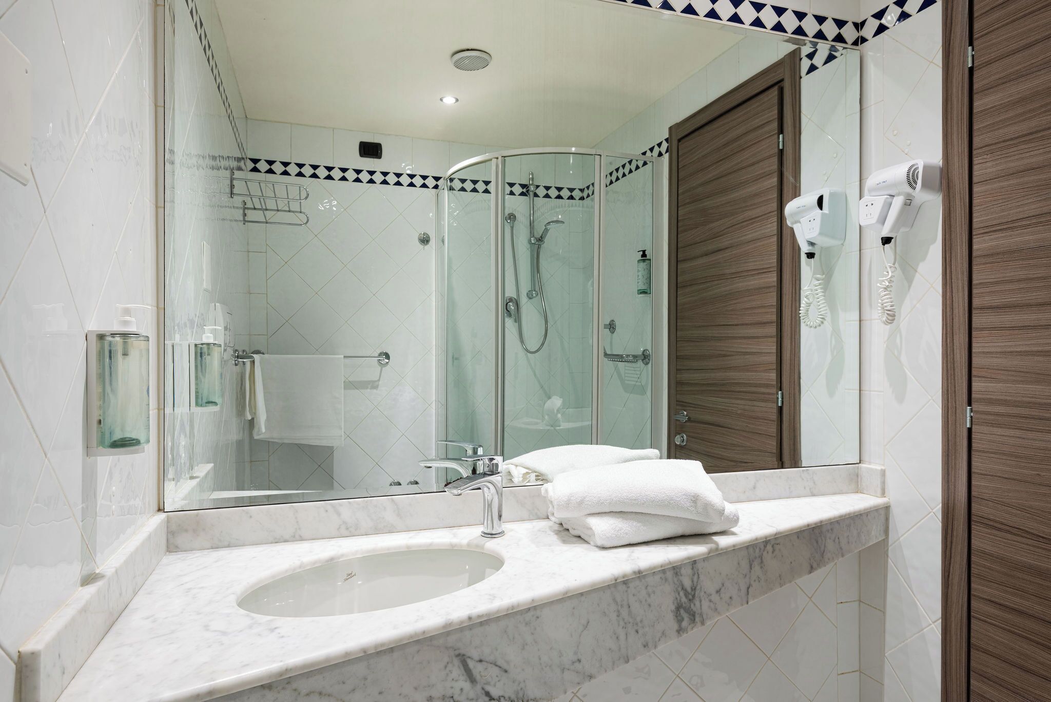 A bathroom with a glass-enclosed shower, a sink with a mirror, and a towel rack.
