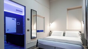 A modern hotel room with a large bed, a bedside table, a mirror, and a door leading to a bathroom. - The Gate Hotel (Sesto Fiorentino)