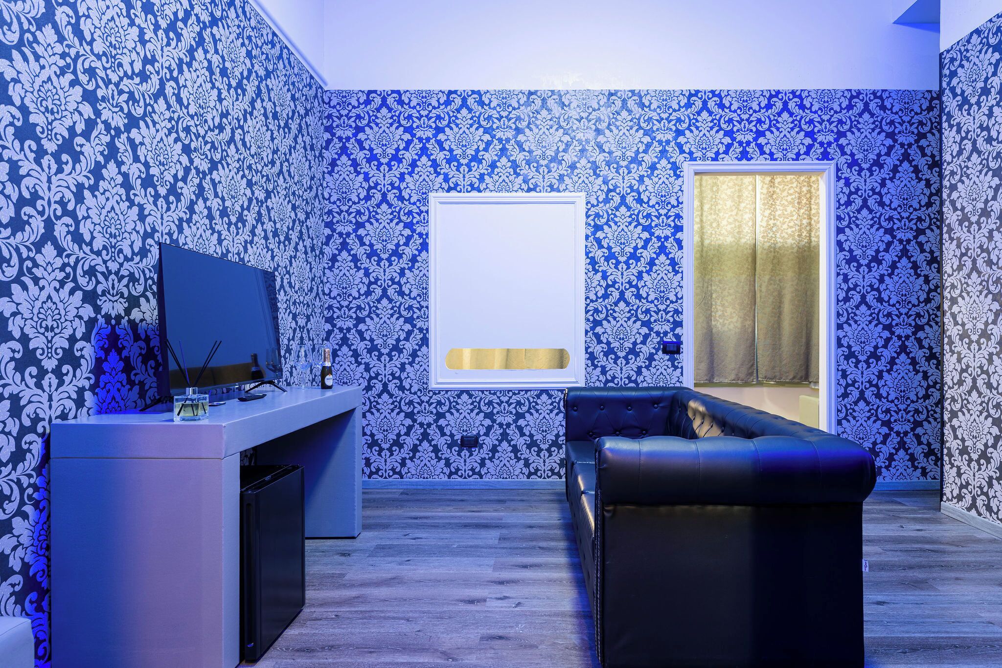 Ein modernes Wohnzimmer mit gemustertem Wandpapier, einem schwarzen Ledersofa, einem Flachbildfernseher und einem kleinen Tisch mit einer Glasvase.