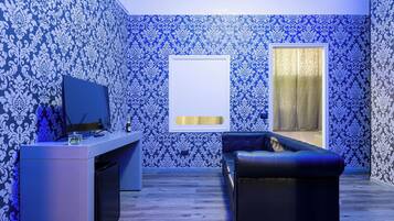 Ein modernes Wohnzimmer mit gemustertem Wandpapier, einem schwarzen Ledersofa, einem Flachbildfernseher und einem kleinen Tisch mit einer Glasvase.