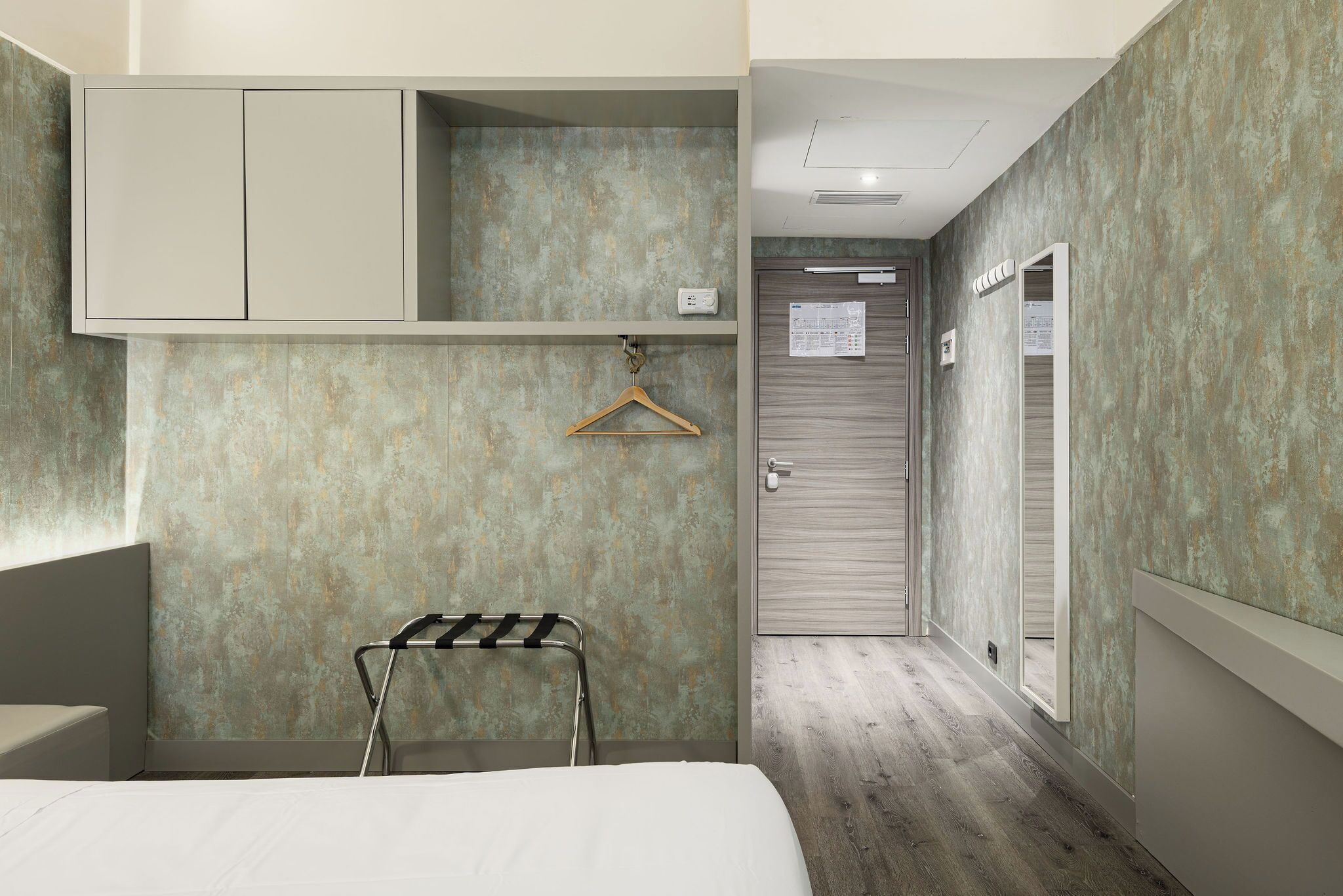 Habitación de hotel con cama, perchero, armario y puerta con un cartel.