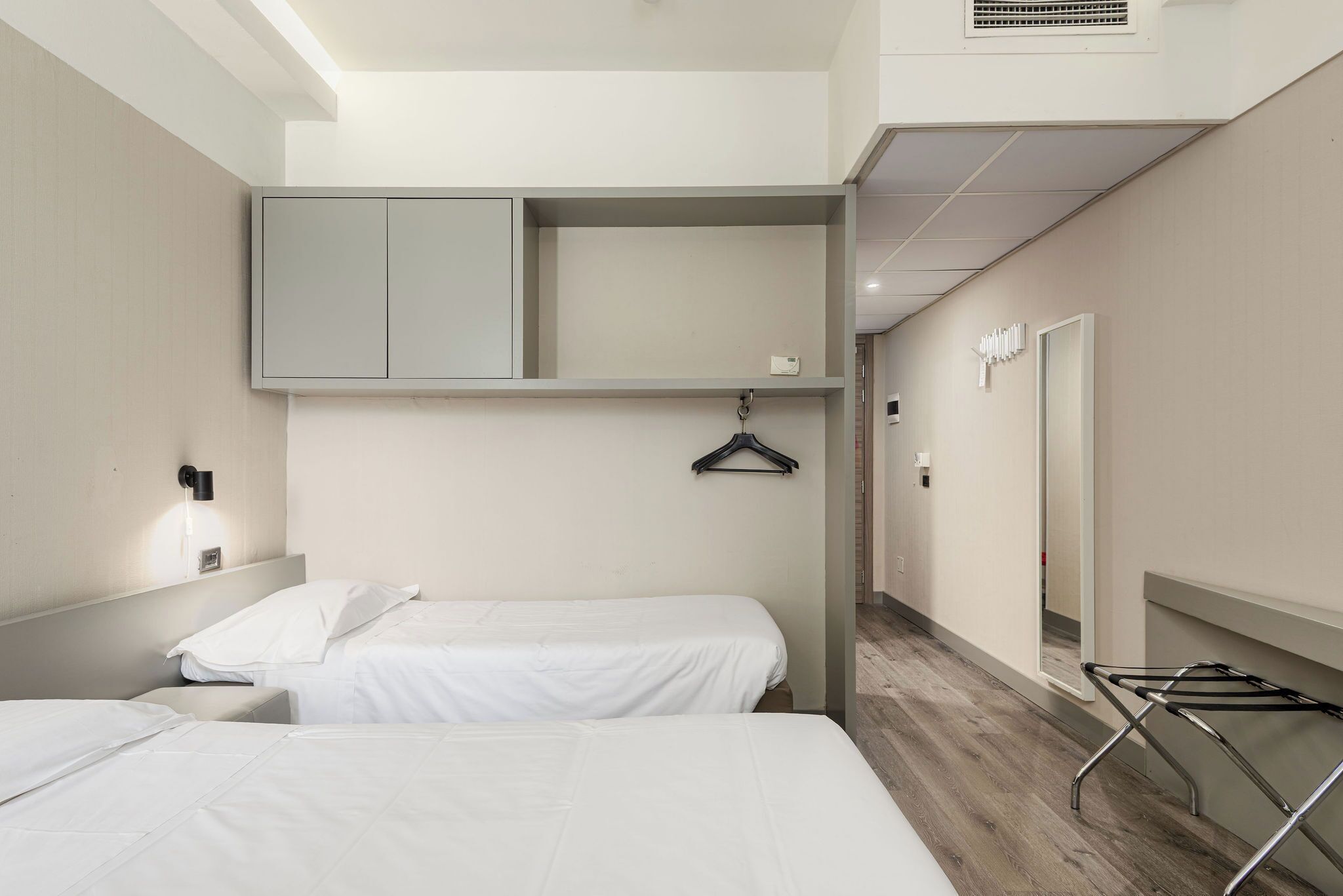 Quarto de hotel com duas camas, um guarda-roupa, um cabideiro e um espelho.